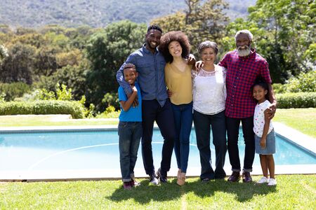 Multi-generation mixed race family enjoying their time at a garden with a pool, standing by the...