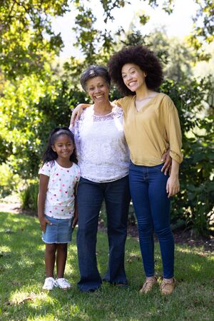 Multi-generation mixed race family enjoying their time at a garden, standing on the grass, embracing, looking at the camera and smilingの写真素材