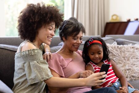 Multi-generation mixed-race family enjoying their time at home together, sitting on a couch,...