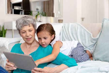 Senior Caucasian woman spending time at home together with her granddaughter, sitting on a couch in...