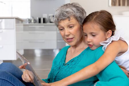Senior Caucasian woman spending time at home together with her granddaughter, sitting on a couch in...