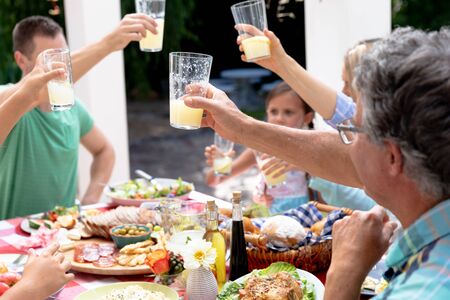 Caucasian three generation family spending time together in the garden on a sunny day, sitting by a table, having a lunch and making a toast with lemonade.の写真素材