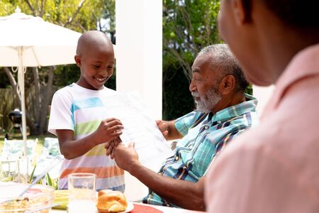 African American boy showing his grandfather his homework during a family lunch in the garden on a sunny day.の写真素材