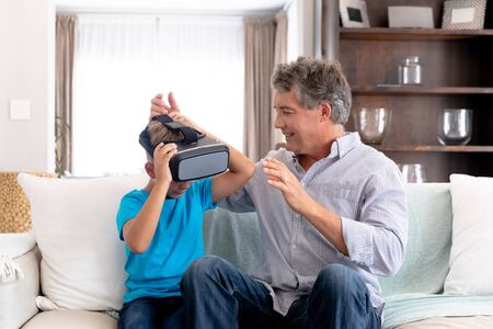 Senior Caucasian man spending time at home together with his grandson, sitting on a couch in the...