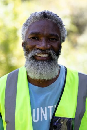 Portrait of a senior African American man standing in a garden, wearing blue volunteer t shirt,...