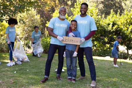 Mixed race boy spending time outside with his family, holding a volunteer sign with his father and...