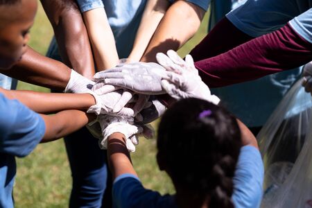 Multi-generation mixed race family spending time outside together, all wearing blue volunteer t shirts and protective gloves, collecting garbage, standing in a huddle, hand stacking, on a sunny dayの写真素材