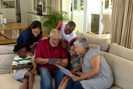 High angle view of a multi-generation mixed race family at home in the living room, gathered together on a couch using a digital tablet, laptop computer and smartphone together and smilingの写真素材