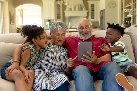Front view of a senior mixed race couple at home in the living room, sitting on the couch with their...