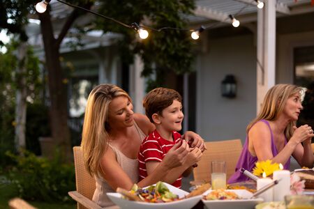 Side view of a multi-generation Caucasian family outside at a dinner table for a celebration meal,...