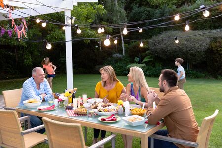Side view of a Caucasian multi-generation family in the garden, the adults sitting at a table for a...
