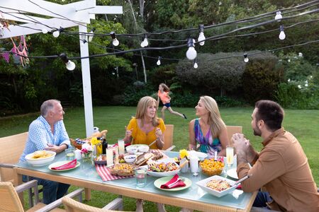 Side view of a Caucasian multi-generation family in the garden, the adults sitting at a table for a...