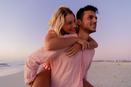 Caucasian couple enjoying time at the beach, a man is holding a woman piggy backの写真素材