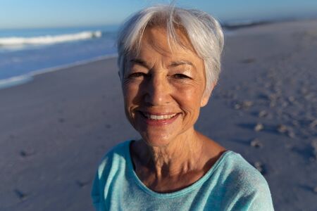 Portrait of a senior Caucasian woman enjoying time at the beach, looking at the camera and smilingの写真素材