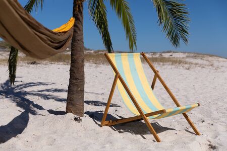Magnificent view of a beach with a deck chair, a palm tree and a hammock tied to itの写真素材