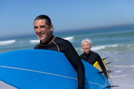 Senior Caucasian couple enjoying time at the beach on a sunny day, walking and holding surfboards with sea in the backgroundの写真素材