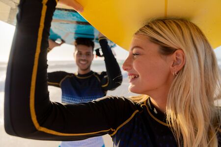 Caucasian couple enjoying time at the beach on a sunny day, holding surfboards above their heads...