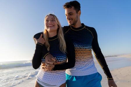 Caucasian couple enjoying time at the beach on a sunny day, walking and holding hands with sea in the backgroundの写真素材
