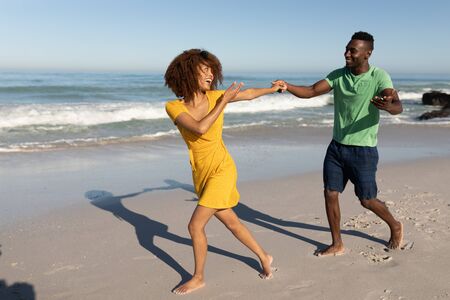 A mixed race couple enjoying free time on beach on a sunny day together, holding hands, having fun...