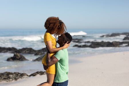 A mixed race couple enjoying free time on beach on a sunny day together, hugging, having fun, hugging and laughing with sun shining on their faces. Relaxing summer vacation.の写真素材