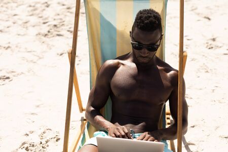 An attractive African American man enjoying free time on beach on a sunny day, sitting in a deck...
