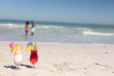 A mixed race couple enjoying free time on beach on a sunny day together with cocktails standing on the sand in the foreground.の写真素材