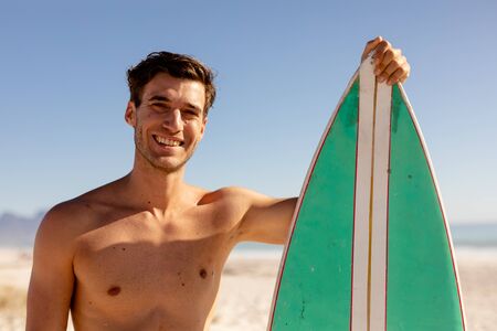 Caucasian man enjoying his time at the beach with his friends on a sunny day, standing shirtless,...