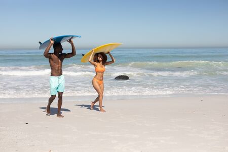 A mixed race couple enjoying free time on beach on a sunny day together, surfing, carrying their surfboards, having fun with sun shining on their faces.の写真素材