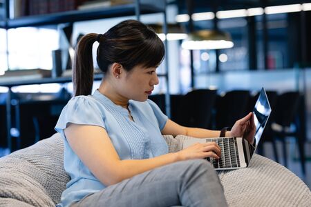 Side view of an Asian businesswoman wearing smart clothes, working in a modern office, sitting on a...