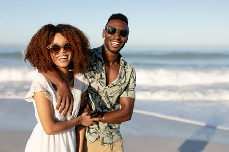 A portrait of a mixed race couple enjoying free time on beach on a sunny day together, walking and...