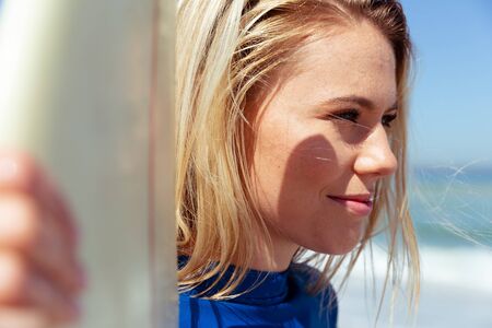 Close up of a Caucasian woman enjoying time at the beach on a sunny day, holding a surfboard and...