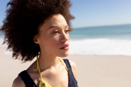Close up of a mixed race woman with afro hairtsyle, on holiday, enjoying free time walking on a sunny beach, with blue sky and sea in the backgroundの写真素材
