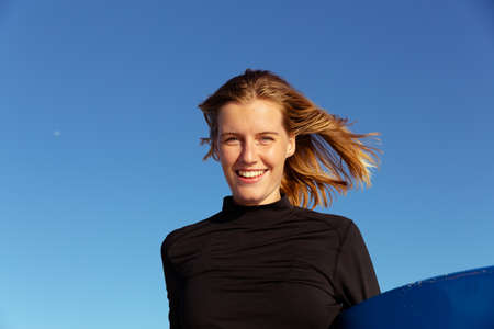Portrait of attractive blonde Caucasian woman enjoying time at the beach on a sunny day, holding...