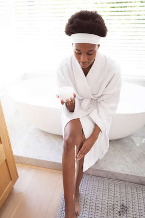 Mixed race woman spending time at home self isolating and social distancing in quarantine lockdown during coronavirus covid 19 epidemic, taking care of her legs skin in her bathroom.の写真素材