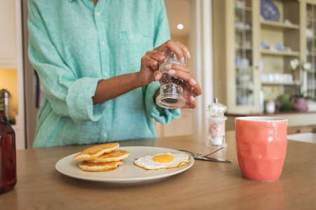 Mid section of a mixed race woman, spending time at home in her kitchen, preparing breakfast. Self isolating and social distancing in quarantine lockdown during coronavirus covid 19 epidemic.の写真素材
