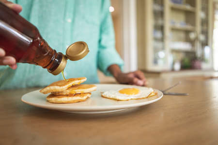 Mid section of a mixed race woman, spending time at home in her kitchen, preparing breakfast. Self isolating and social distancing in quarantine lockdown during coronavirus covid 19 epidemic.の写真素材