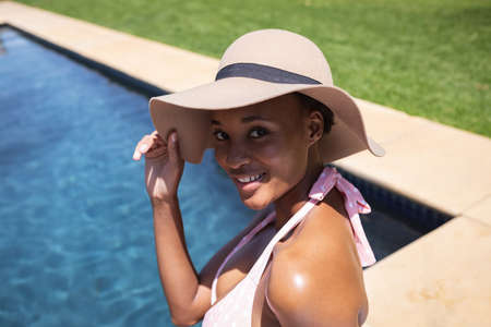 Mixed race woman spending time at home, relaxing and sunbathing by the pool. Self isolating and...