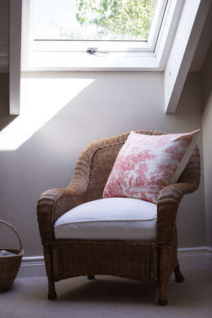 Modern room interior showing a wicker sofa chair with a patterned pillow on it standing in the corner  of the room with a window above it showing green trees. Luxury apartament interior design.の写真素材