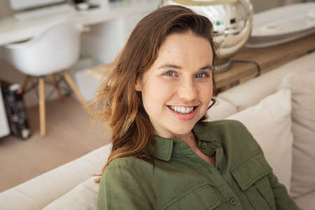 Portrait of a happy, attractive Caucasian woman spending time at home, sitting on sofa. Lifestyle at...