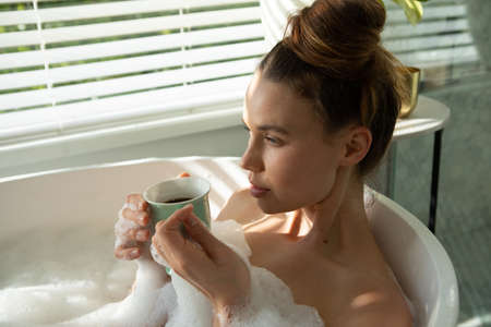 A Caucasian woman spending time at home, having a foamy bath, drinking coffee. Lifestyle at home...