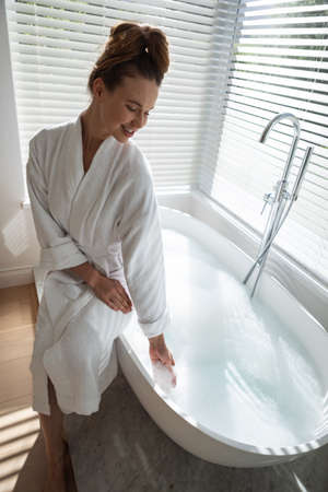 A Caucasian woman spending time at home, wearing a bathrobe, sitting on the bathtub. Lifestyle at...