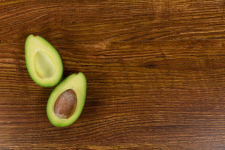 Top view of a fresh green avocado with a pit, cut in half and arranged on a textured wooden surface