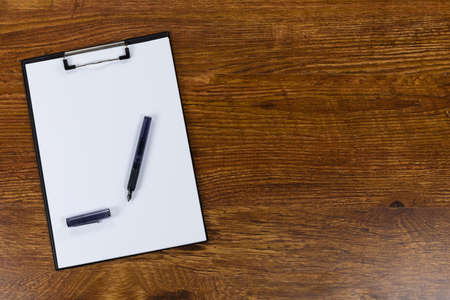 Close up top view of a clipboard with an empty sheet of paper and a black pen arranged on a textured...
