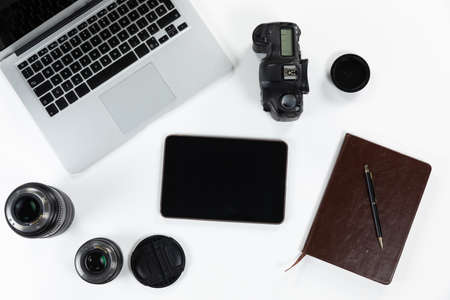 Close up top view of a notebook, a pen, a laptop, a tablet, a camera and lenses in various sizes...