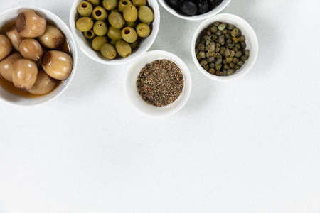 Top view of a six bowls with fresh olives, nuts and seasoning, arranged on a on a plain white surface.の写真素材