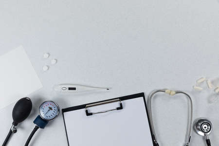 Top view of a composition with medical devices, pills and a folder with an empty sheet of paper, arranged on a plain white surface.の写真素材