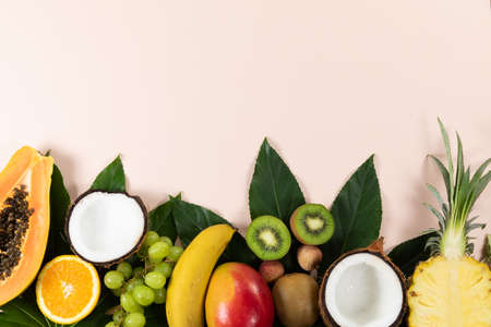 Top view of a composition with variety of fresh tropical fruits and green leafs arranged on a pink...