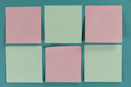 Close up top view of six green and pink sheets of paper sticky memo notes in one size, arranged on a...