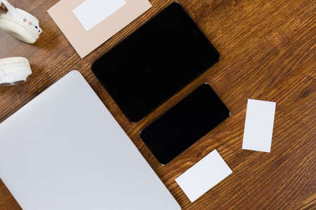 Close up top view of a laptop, a tablet, a smartphone, headphones and sheets of paper in various sizes arranged on a textured wooden surfaceの写真素材