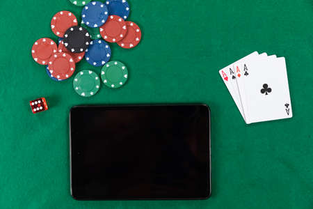 Close up top view of a black tablet, playing cards, a red dice and colorful poker chips, arranged on...